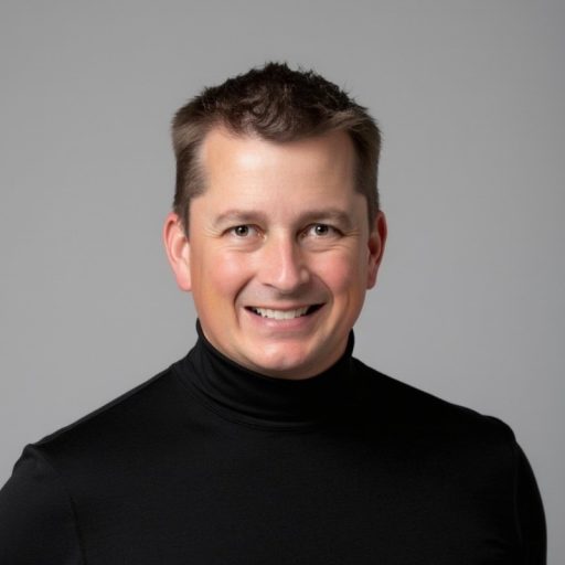 A professional headshot of a man with short brown hair, wearing a black turtleneck, smiling against a neutral gray background.